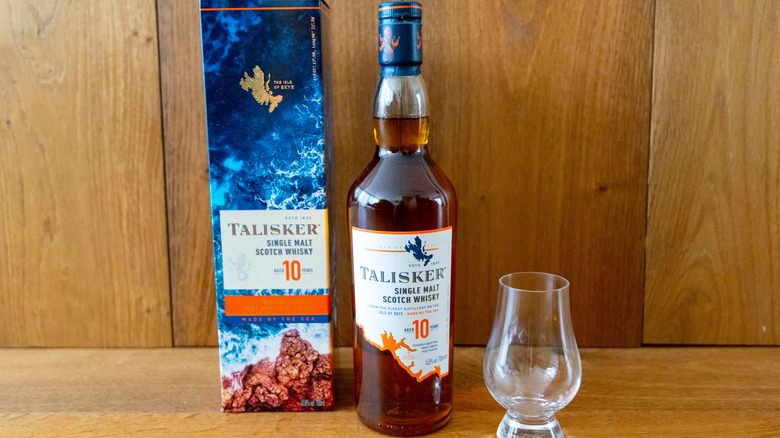 A bottle of Talisker 10-year one a wooden surface with the box on one side and an empty glass on the other