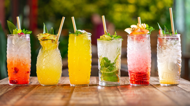 A line of colorful cocktails in clear tiki glasses