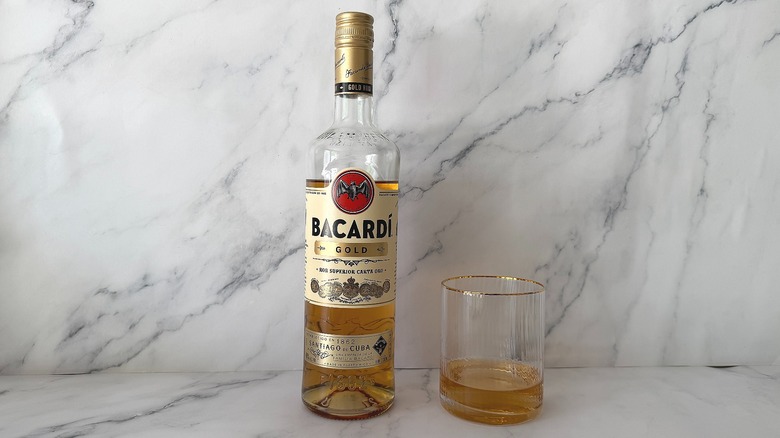Bacardi Gold bottle next to glass of Bacardi Gold on marble surface