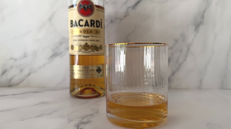 Glass of Bacardi Gold, bottle in background on marble surface