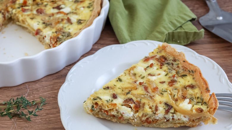 a slice of bacon, onion, and goat cheese quiche on a plate