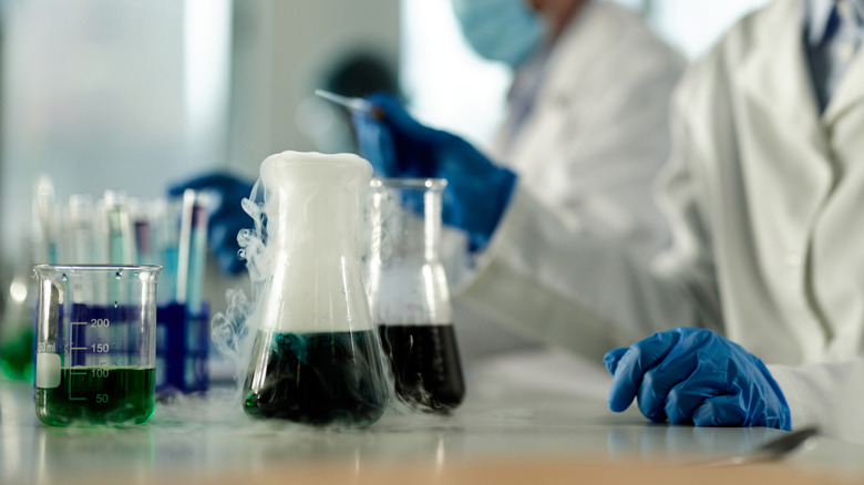 Blue-gloved scientists handling beakers of smoking liquid
