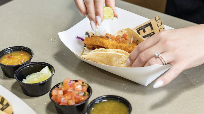 Baja Fresh customer squeezing lime onto taco next to salsa containers