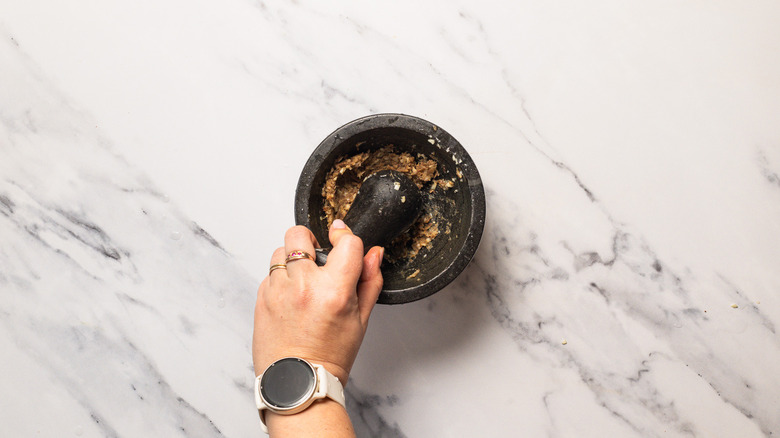 Mashing anchovies and garlic in a mortar.