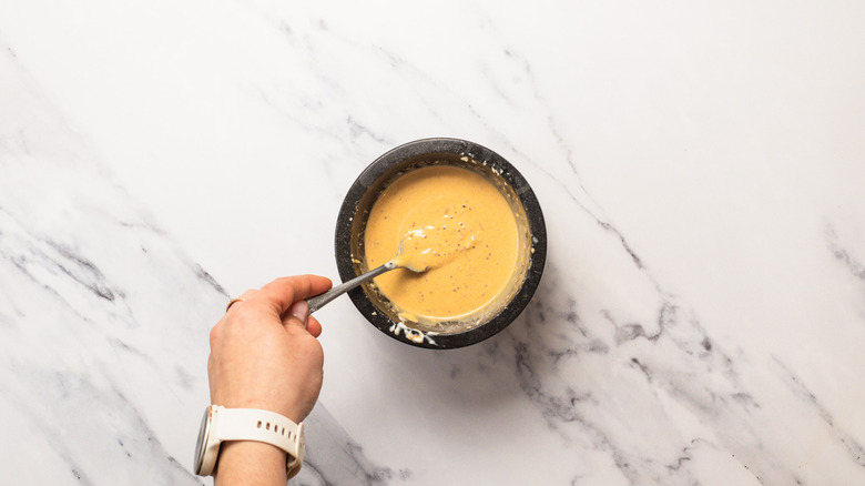 Whisking Caesar salad dressing in a mortar with a fork.