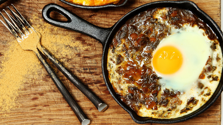 egg baked into a skillet of dal on a wood table