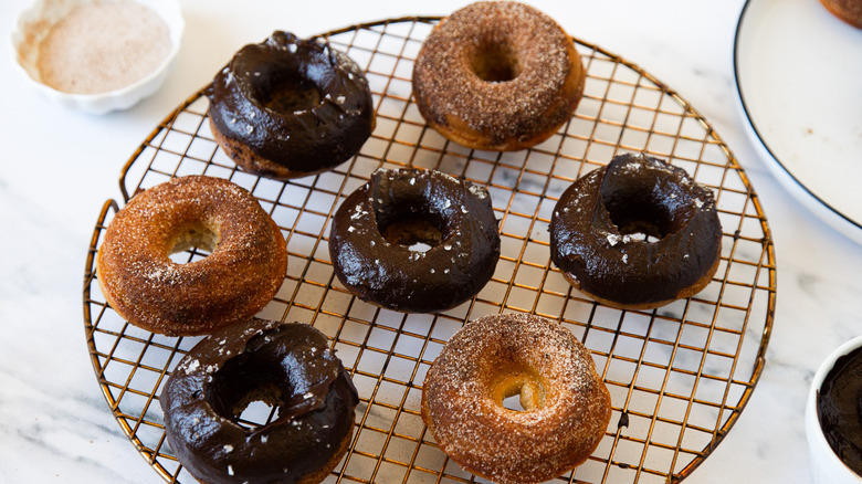 Chocolate and cinnamon sugar baked churro cake donuts on a round drying rack.