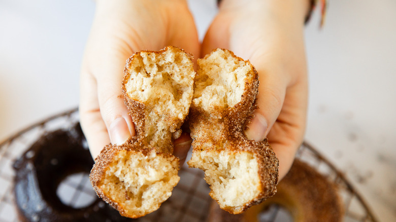 Two hands holding a cake donut cut in half.