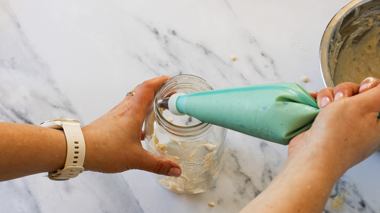 Hand holding piping bag with batter over jar.