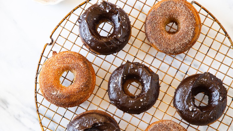 Chocolate and cinnamon sugar baked churro cake donuts on a round drying rack.