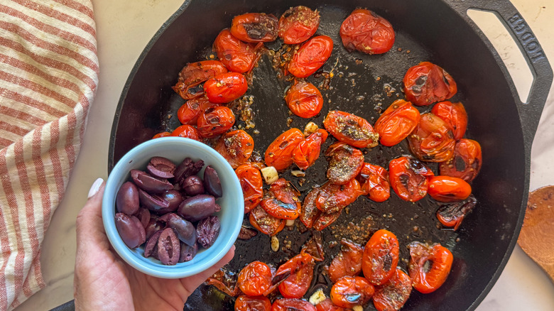 hand adding olives to skillet