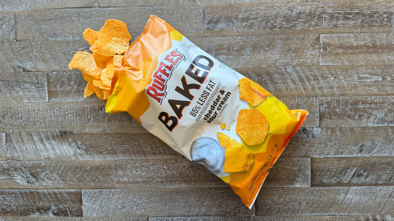 Ruffles baked cheddar and sour cream potato chips bag with chips spilling out on a wooden surface