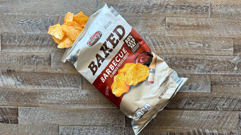 Clancy's baked barbecue potato chips bag with chips spilling out on wooden surface