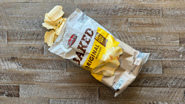 Clancy's baked original potato chips bag with chips spilling out on wooden surface