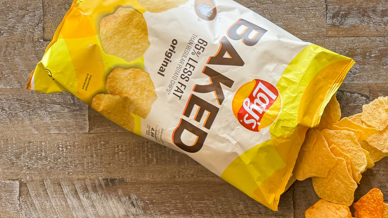 Three bags of Lay's potato chips with chips spilling out on a wooden surface