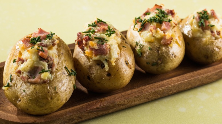 A wooden plate holding four loaded baked potatoes