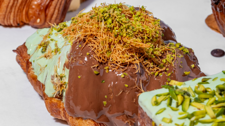 Close-up of a Dubai chocolate croissant topped with crispy knafeh and chopped pistachios
