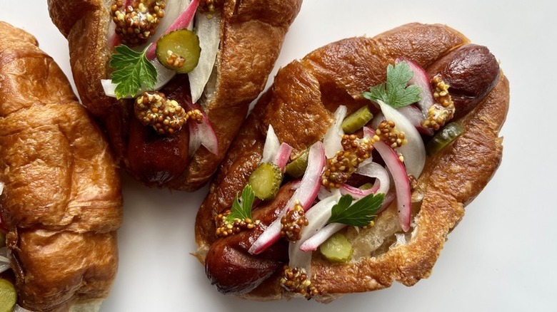 Croissants stuffed with hot dog sausages, sliced onion, mustard, and pickles