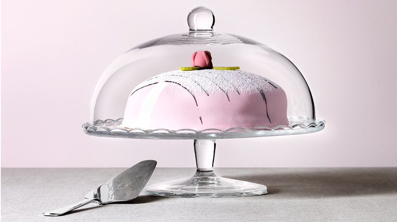 A pink cake in a glass cake stand