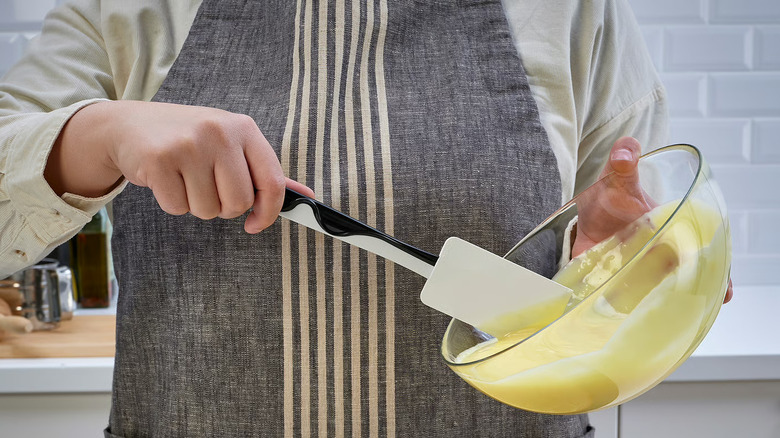 A baker scraping pastry cream from a bowl with a rubber spatula