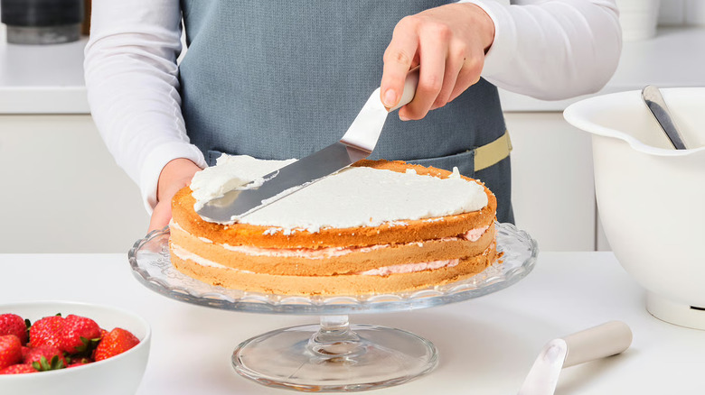 A baker spreading frosting on a cake with an offset spatula