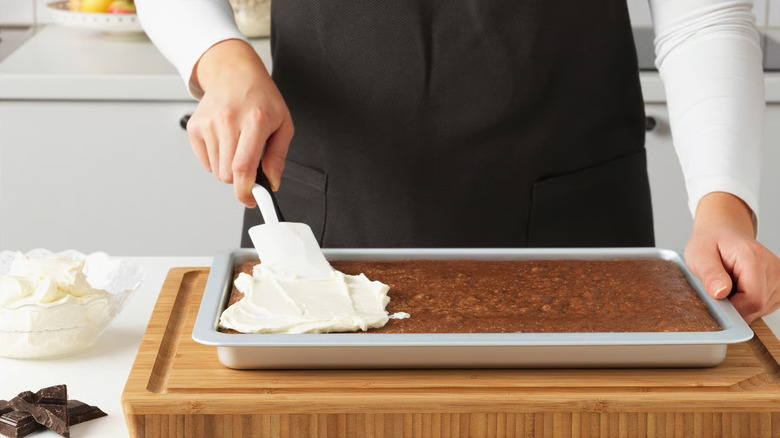 A baker spreading frosting on a tray of brownies