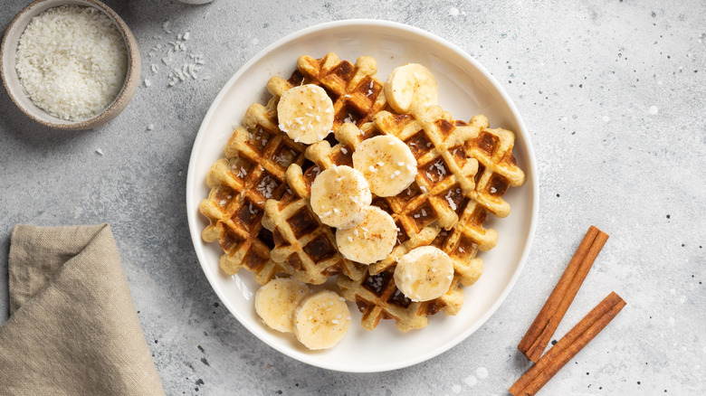 Waffles topped with fresh banana slices on white plate