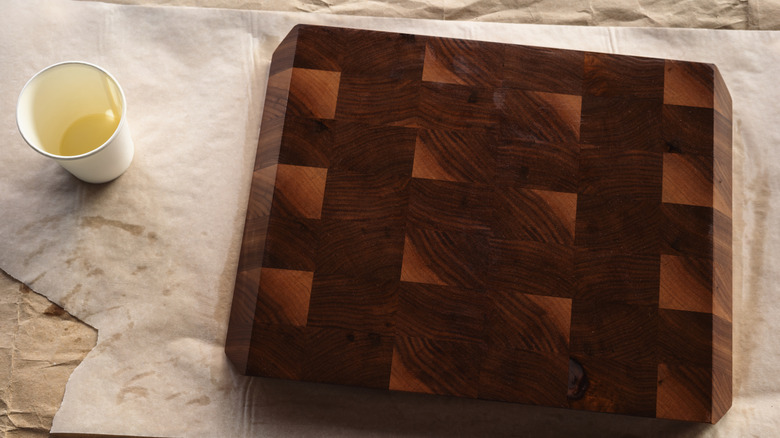 A cup of oil next to a wooden cutting board that is being seasoned