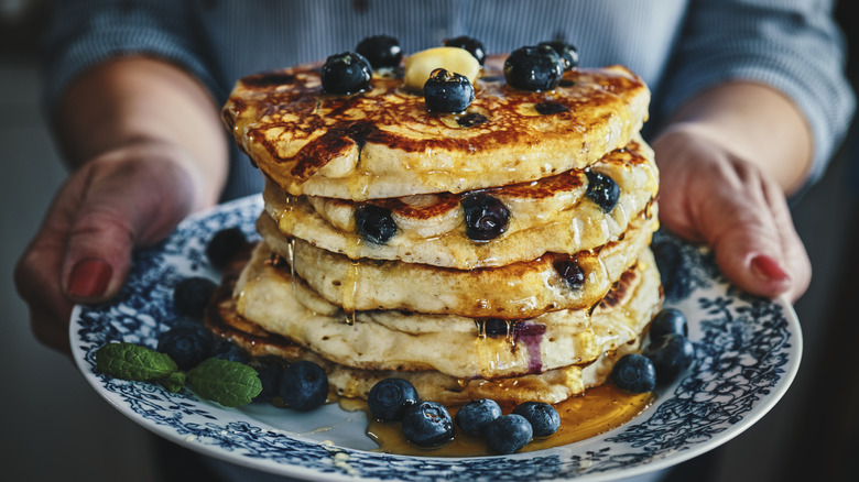 hands holding stack of blueberry pancakes