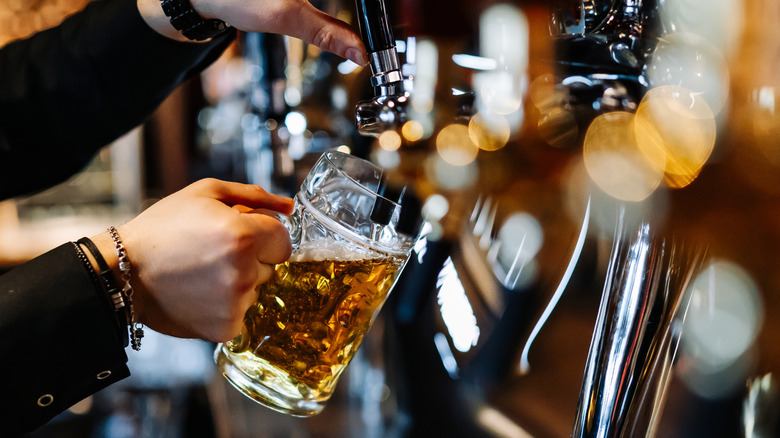 The hands of a bartender pours a pint of draft beer into a handled glass beer mug