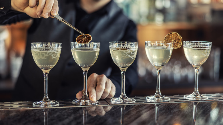 Bartender pacing dried lime garnishes on row of cocktails