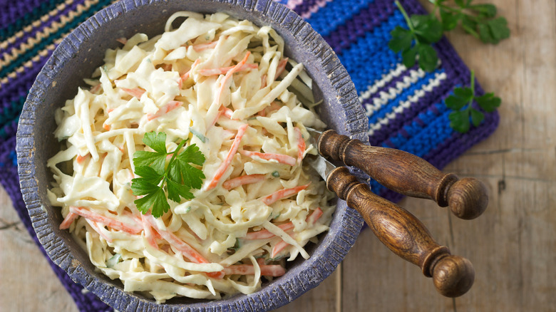 Coleslaw sits in a bowl on a wooden table with a blue crocheted napkin underneath