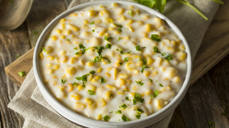 A bowl of creamed corn sits on a napkin on a wooden table