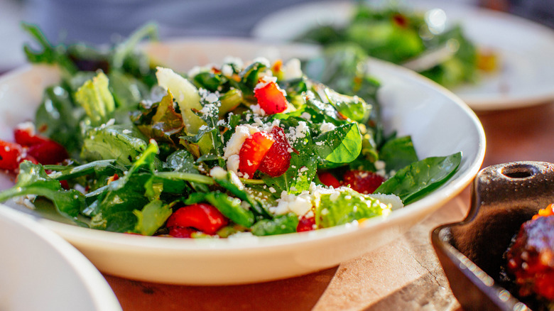 A white bowl hols a green salad with spinach, strawberries, and cheese