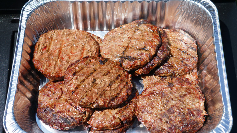 a large quantity of grilled burger patties left sitting in a foil baking pan