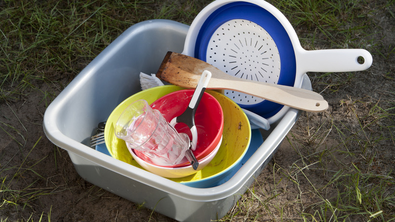 a plastic basin filled with dirty dishes, sitting on thin, dry grass