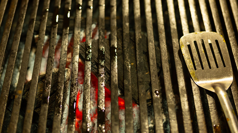 closeup image of a dirty grate over a bed of hot coals, with a metal spatula resting on the right side of the grate