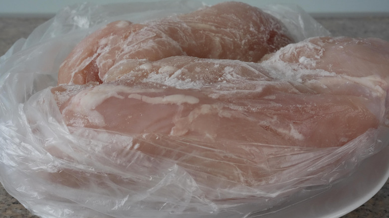 closeup image of frozen chicken breasts in a plastic bag, defrosting at room temperature on a plate on the counter