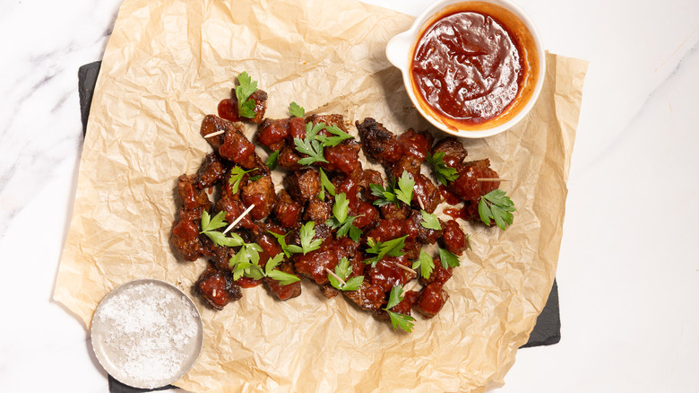 Steak bites on tray with parchment paper next to sauce and salt