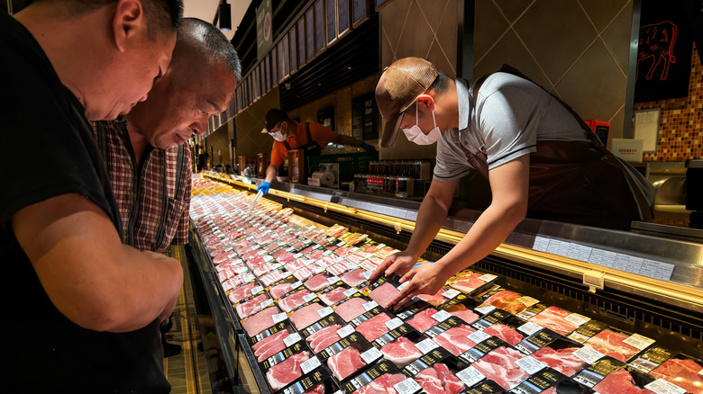 two customers look at the meat section of a grocery store while a worker holds a package