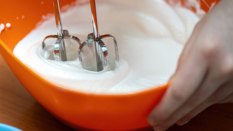 An electric mixer beating eggs into a white foam inside a red mixing bowl