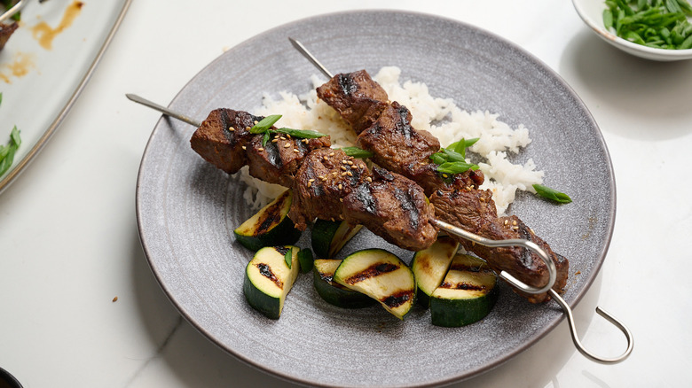 beef kebabs on a plate with rice and vegetables