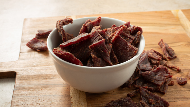 A bowl of beef jerky chunks overflowing onto a wooden cutting board