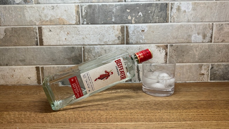 bottle of Beefeater gin leaned over onto a glass of gin on the rocks