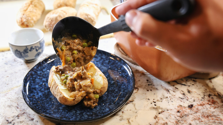 Ladle pouring beefy gravy into the center of a split jacket potato