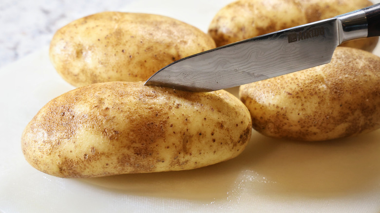 a kitchen knife slicing into the top of a russet potato