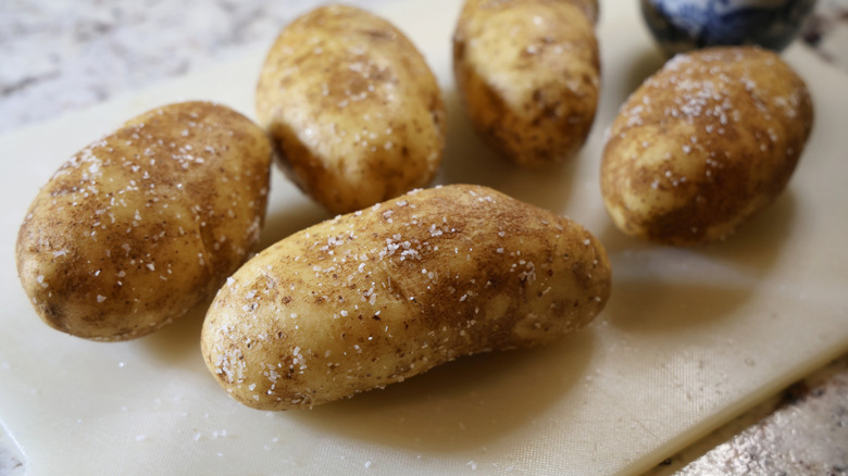 russet potatoes coated with coarse salt on a plastic cutting board