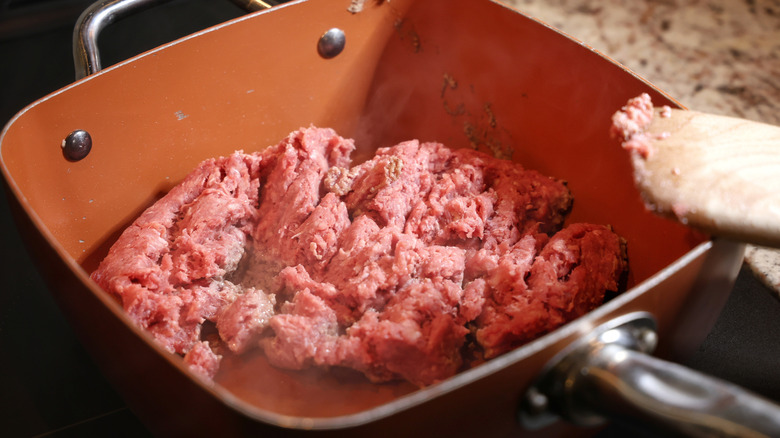 ground beef cooking in an orange pan with a wooden spatula resting on the edge