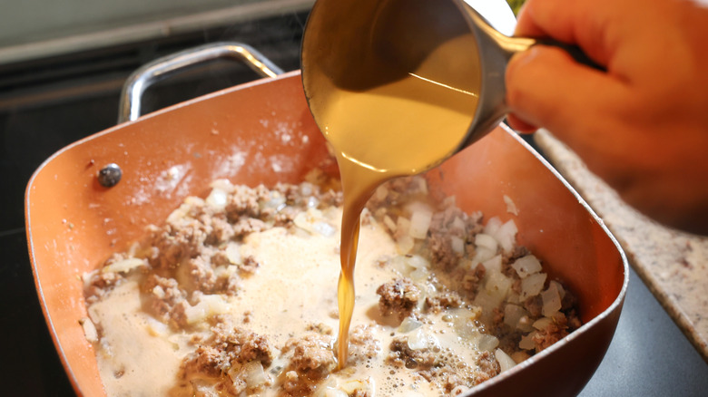measuring cup of stout beer pouring into pan of cooked ground beef and onions