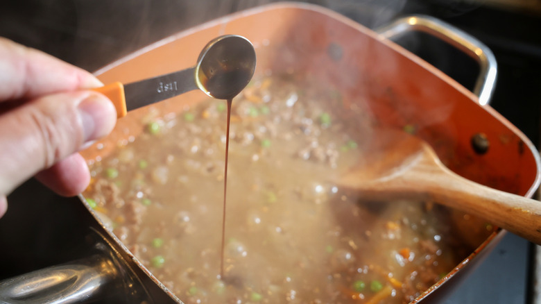 measuring spoon of Worcestershire sauce pouring a thin stream into a pan of beef and vegetables in gravy